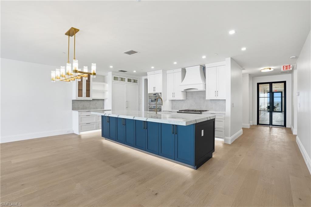 Kitchen with dual tone cabinets, a large island, backsplash, light wood-style flooring, and open shelves
