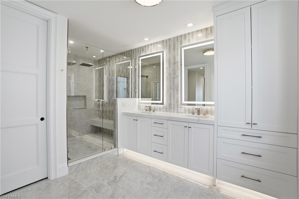 Full bath with double vanity, a shower stall, recessed lighting, and light marble finish floors