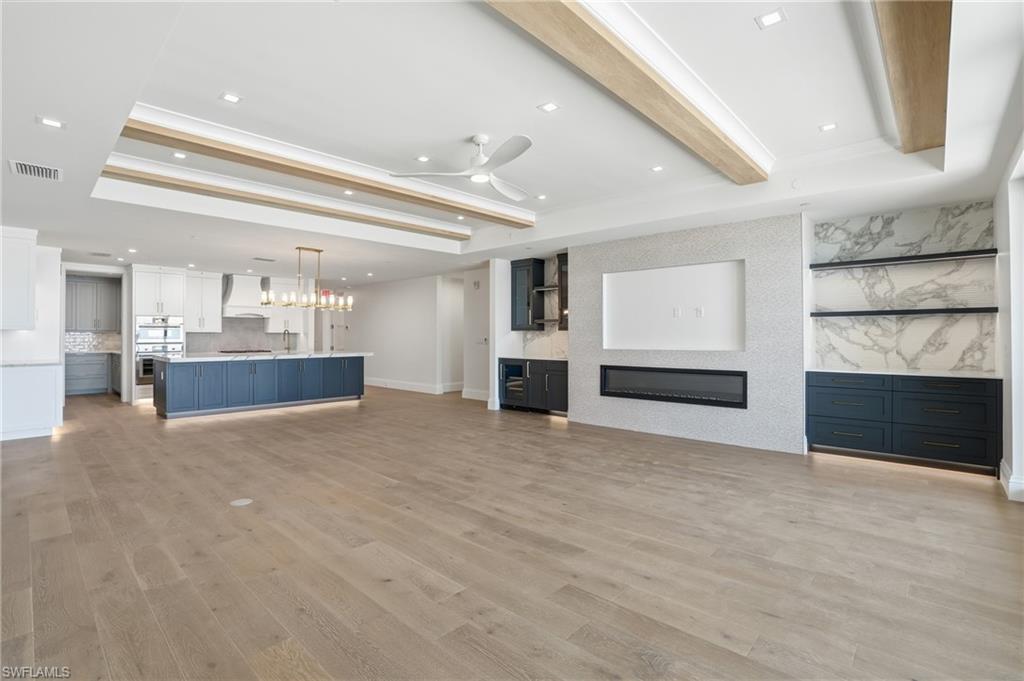 Unfurnished living room with a glass covered fireplace, a ceiling fan, a raised ceiling, light wood finished floors, and beamed ceiling