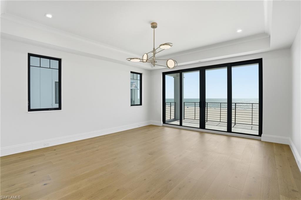 Empty room with a raised ceiling, a chandelier, light wood-type flooring, a water view, and ornamental molding