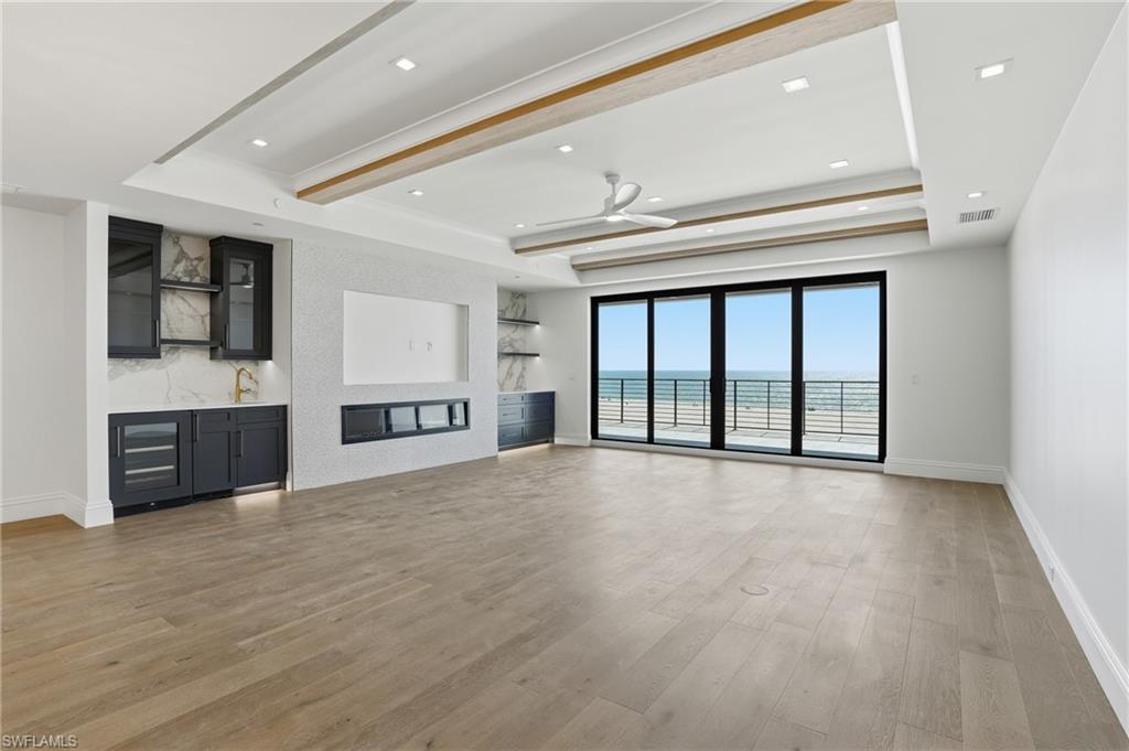 Unfurnished living room featuring light wood-type flooring, a ceiling fan, beamed ceiling, recessed lighting, and a tray ceiling