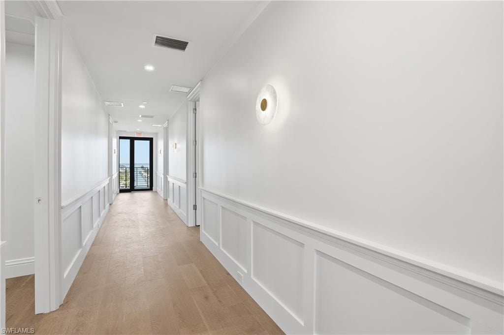 Hall featuring a decorative wall, light wood-type flooring, wainscoting, and recessed lighting