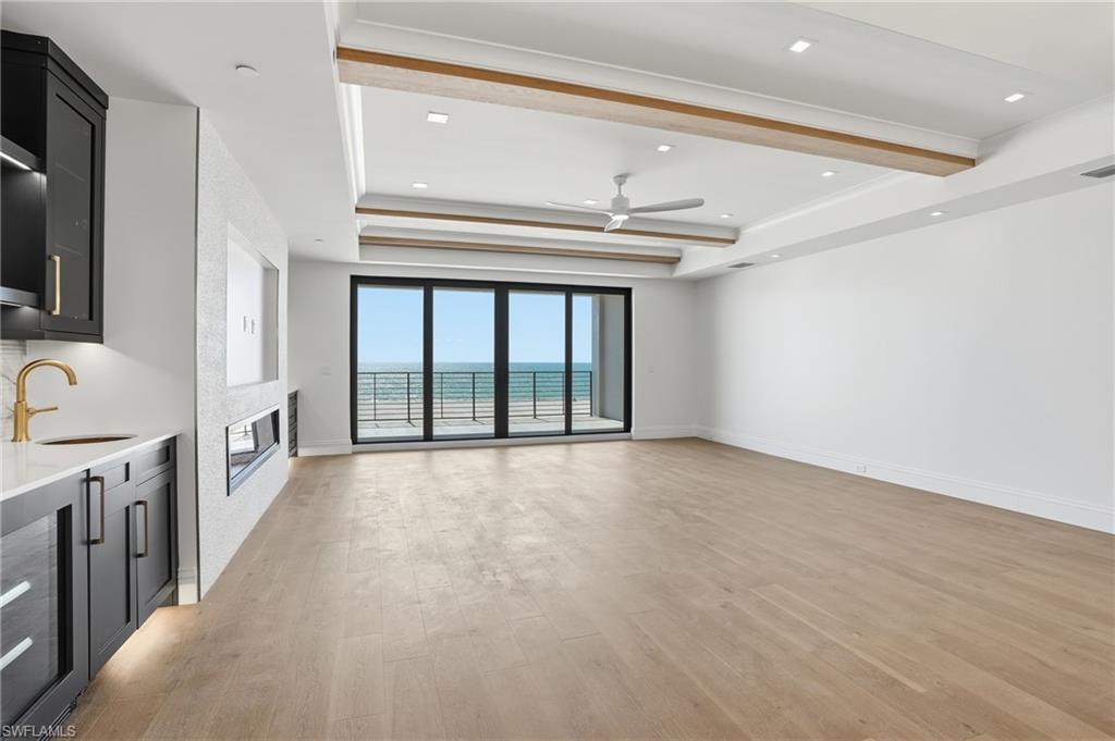 Unfurnished living room with light wood-style floors, a ceiling fan, beverage cooler, a glass covered fireplace, and a tray ceiling
