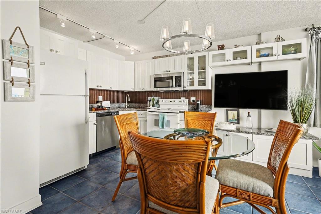 Kitchen featuring stainless steel appliances, white cabinetry, glass insert cabinets, a textured ceiling, and light stone countertops