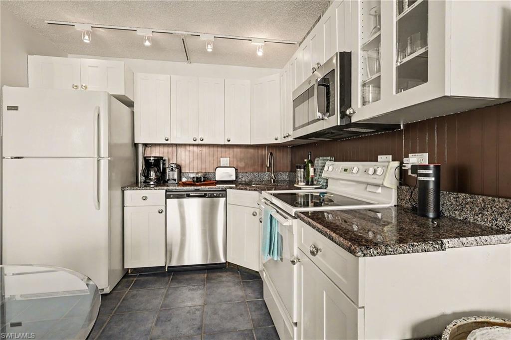 Kitchen featuring stainless steel appliances, white cabinetry, dark stone counters, track lighting, and a textured ceiling