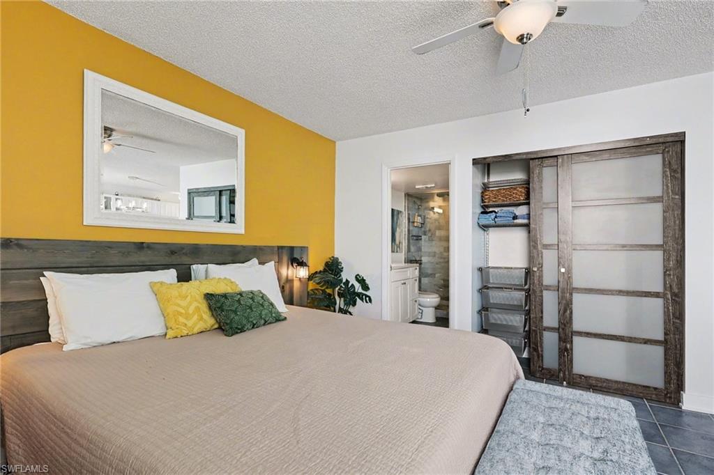 Bedroom with a textured ceiling, ceiling fan, ensuite bath, tile patterned flooring, and a closet
