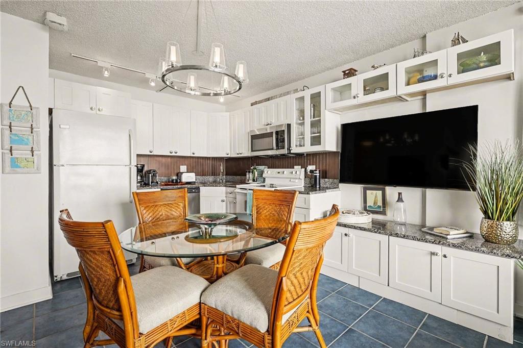 Kitchen with white cabinetry, white appliances, hanging lights, glass fronted cabinets, and dark tile patterned flooring