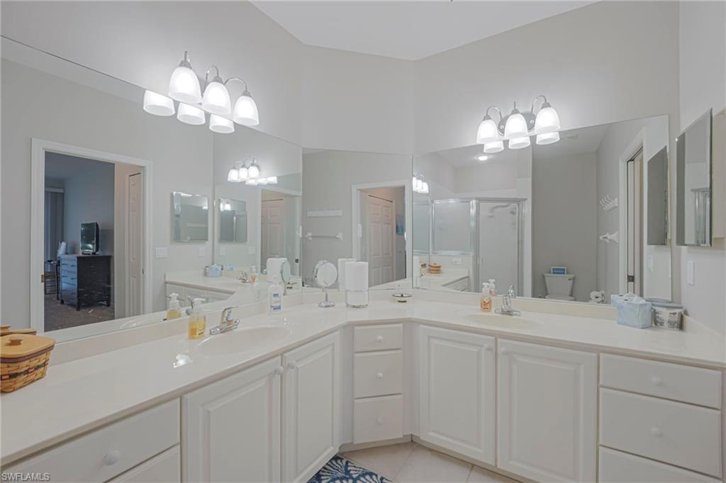 Bathroom featuring double vanity, a shower stall, light tile patterned flooring, and suspended lighting