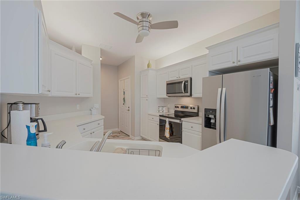 Kitchen featuring stainless steel appliances, light countertops, a ceiling fan, and white cabinets