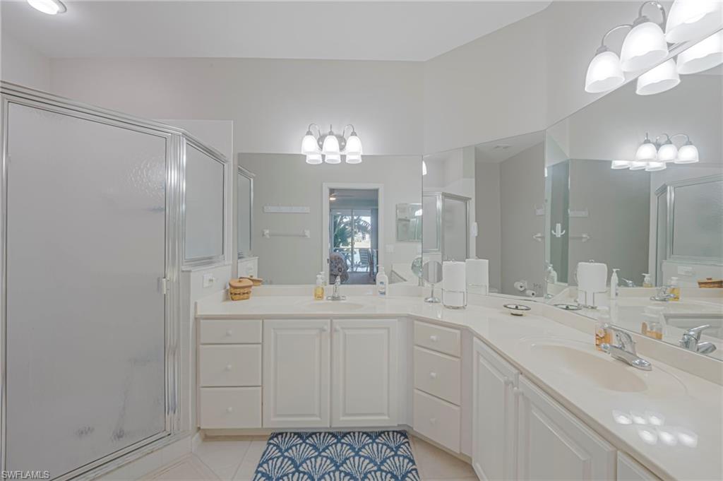 Full bath featuring a shower stall, double vanity, hanging lights, and light tile patterned floors