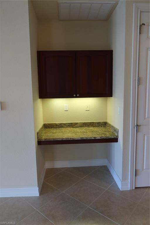 Built-in desk area featuring a stone-finish countertop, under-cabinet lighting, upper cabinetry, and tile flooring