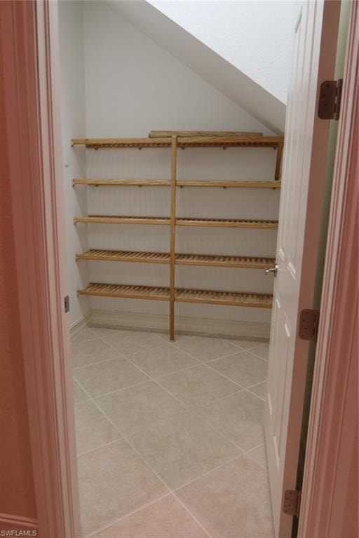 Storage area featuring light-toned tile flooring and multiple slatted wood shelves