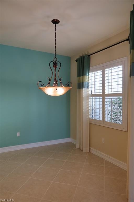 Room featuring neutral tile flooring, white baseboards, and a prominent chandelier with an antique bronze finish and frosted glass bowl