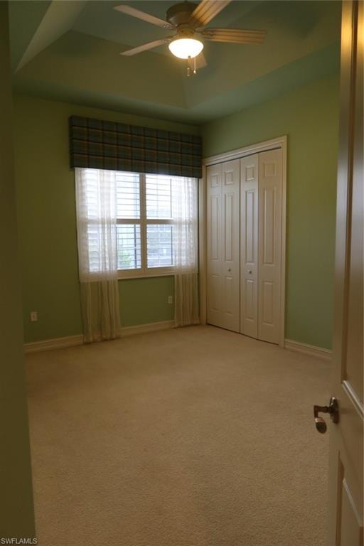 Recessed tray ceiling with ceiling fan, neutral carpet flooring, and bi-fold closet doors