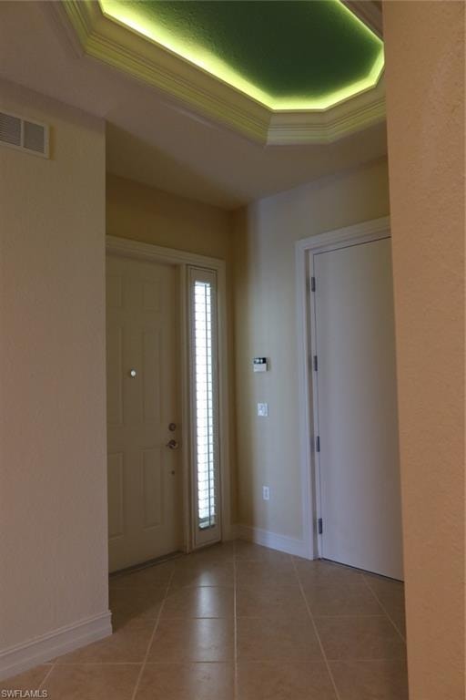 Foyer featuring a decorative tray ceiling with ambient lighting, a solid entry door with a full-length sidelight, ceramic tile flooring, and crisp white baseboards