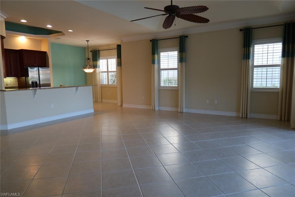 Expansive open-concept living space featuring neutral tile flooring, a tray ceiling with a ceiling fan, and two windows with plantation shutters