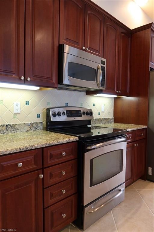 Stainless steel range and microwave oven complementing rich wood-finish cabinetry, granite countertops, and a tile backsplash with decorative accents