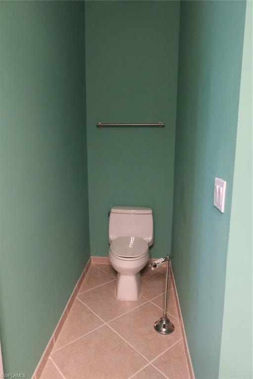 Enclosed water closet featuring a standard toilet, tiled flooring, and a wall-mounted towel bar