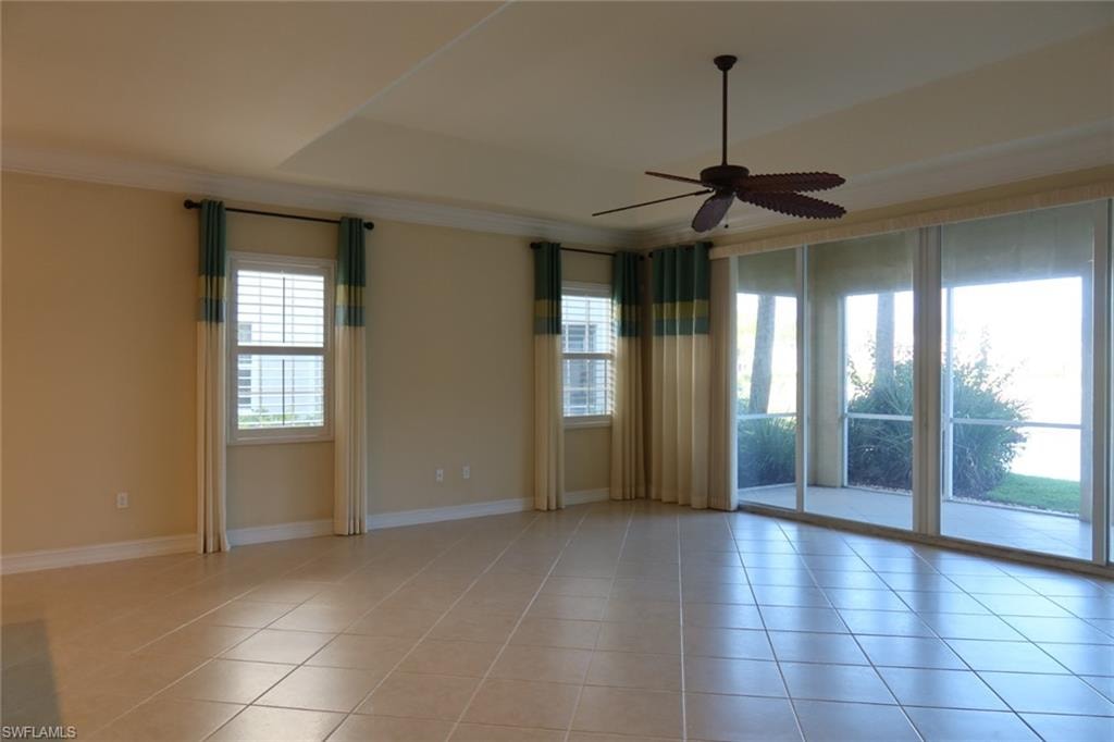 Spacious room featuring neutral tile flooring, a tray ceiling, and a ceiling fan