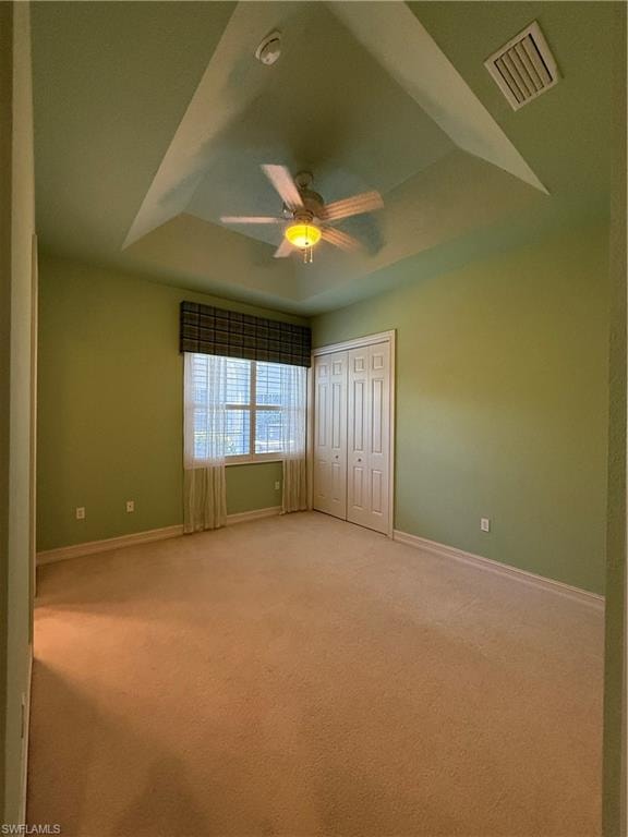 Unfurnished bedroom featuring a tray ceiling, light colored carpet, a closet, and ceiling fan