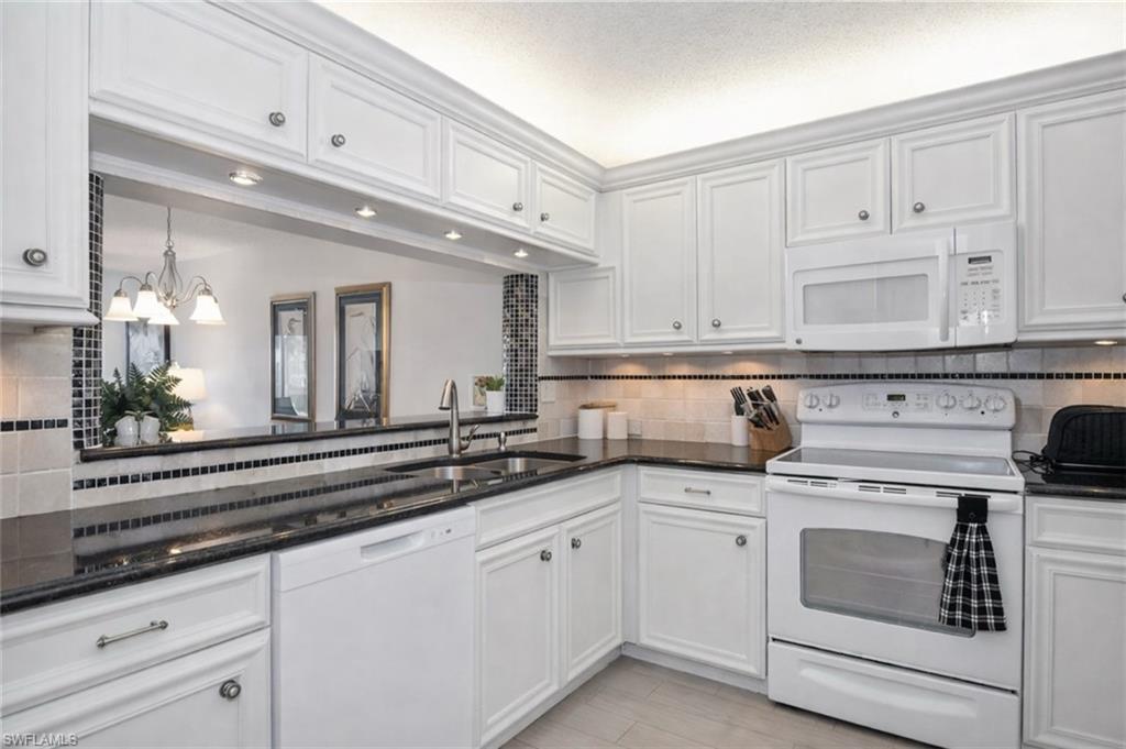 Kitchen with white appliances, dark stone countertops, and white cabinetry