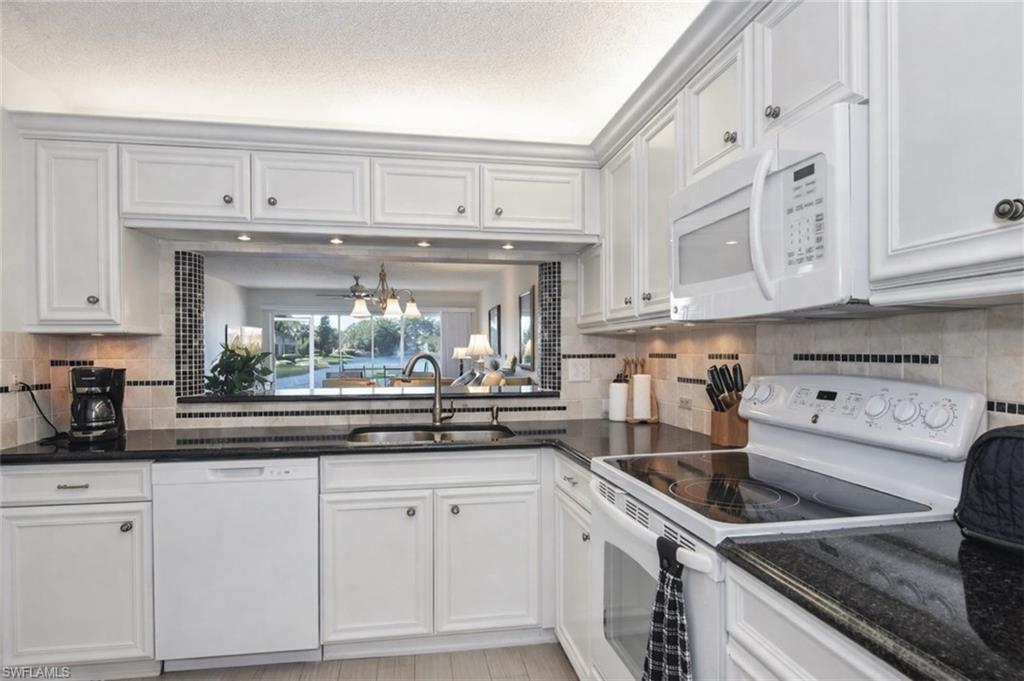 Kitchen with white appliances, white cabinets, dark stone counters, and tasteful backsplash