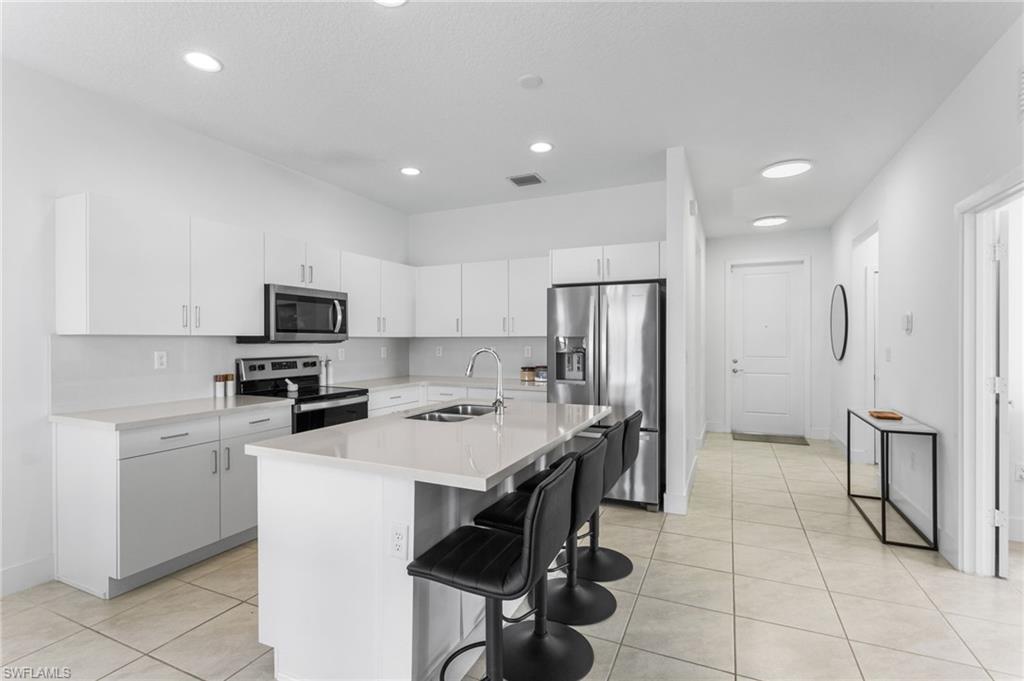Kitchen featuring white cabinets, stainless steel appliances, a breakfast bar area, an island with sink, and light tile patterned floors