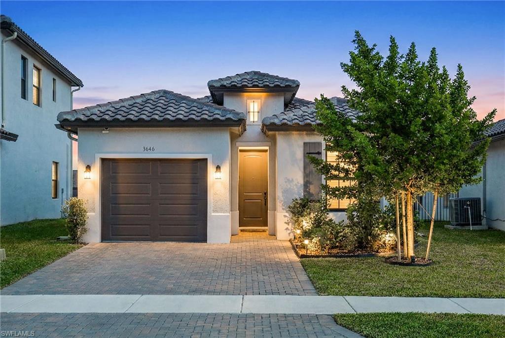 Mediterranean / spanish home with an attached garage, a lawn, decorative driveway, and stucco siding