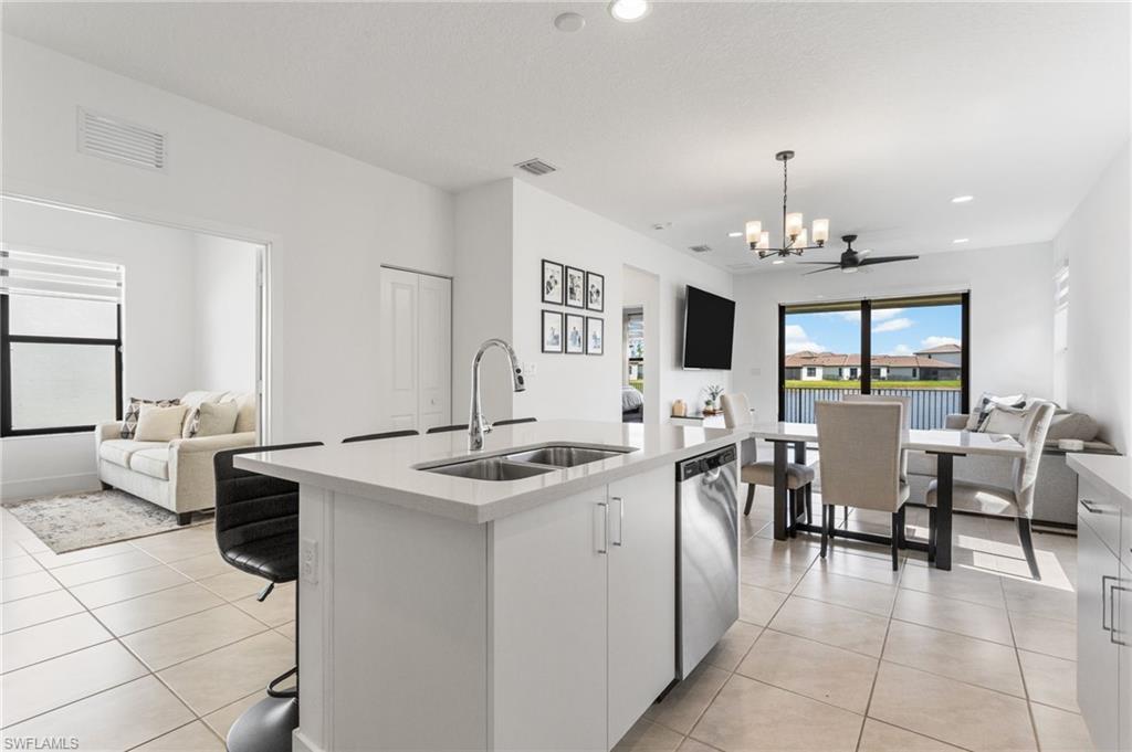 Kitchen featuring open floor plan, an island with sink, light stone counters, suspended lighting, and white cabinets