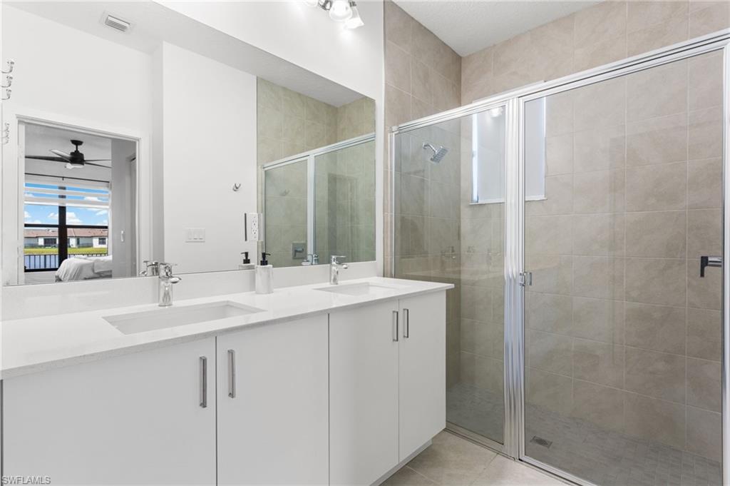 Ensuite bathroom with double vanity, a stall shower, and light tile patterned flooring