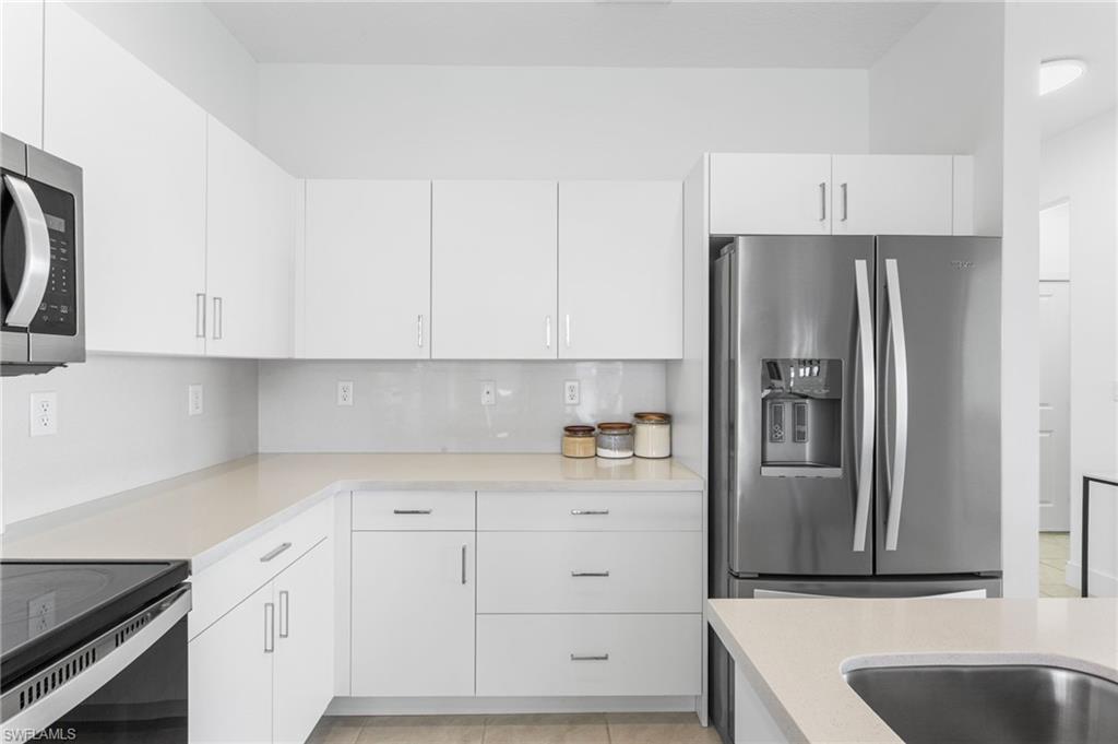 Kitchen featuring stainless steel appliances, white cabinetry, light tile patterned floors, and tasteful backsplash