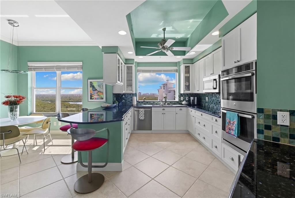 Kitchen featuring glass fronted cabinets, a peninsula, backsplash, white cabinets, and stainless steel appliances