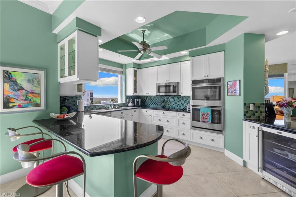 Kitchen with beverage cooler, dark stone counters, white cabinetry, backsplash, and a peninsula