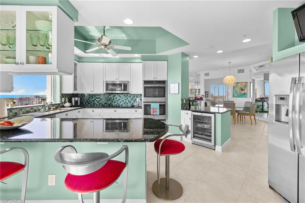 Kitchen featuring a peninsula, white cabinetry, dark stone countertops, glass insert cabinets, and a breakfast bar