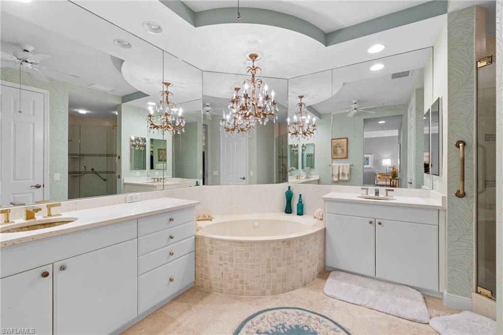 Full bath featuring a ceiling fan, a shower stall, a garden tub, two vanities, and a chandelier