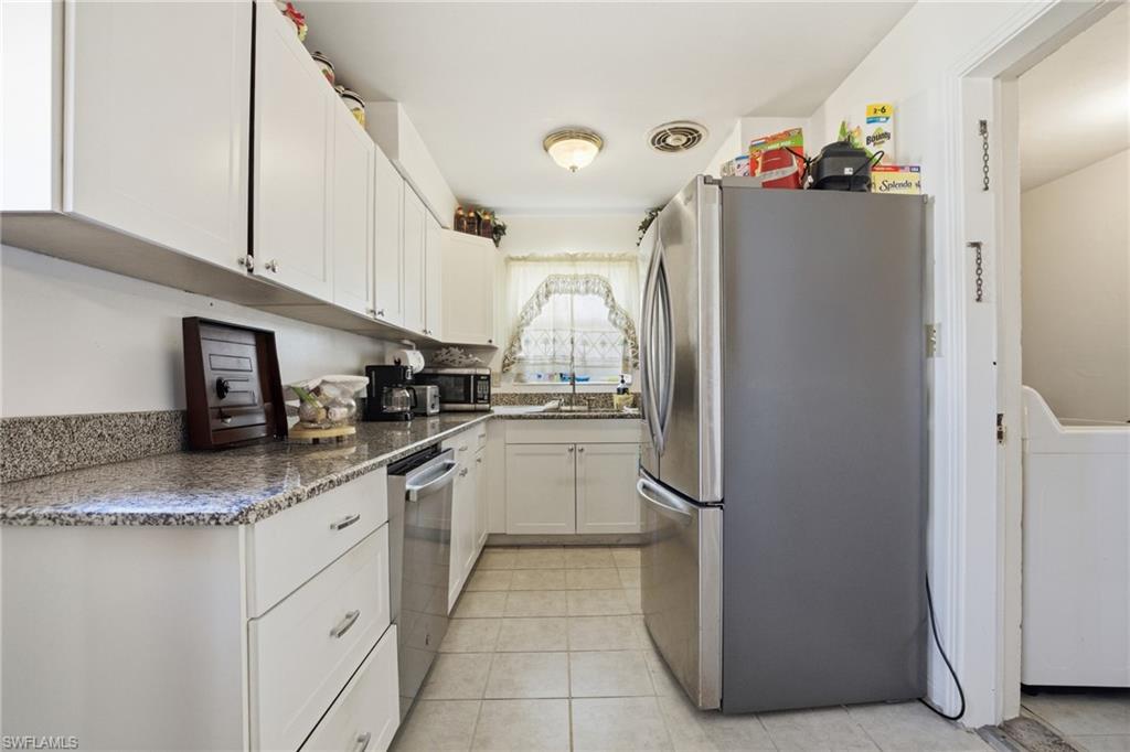Kitchen featuring white cabinets, appliances with stainless steel finishes, dark stone countertops, and washer / dryer