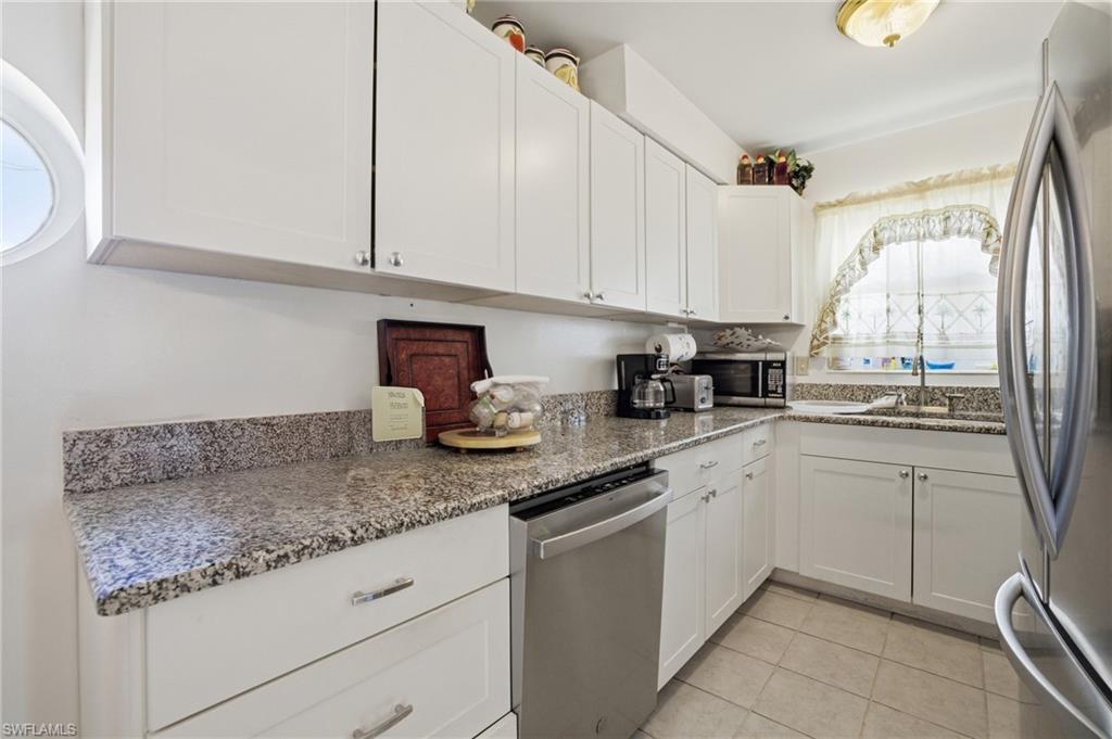 Kitchen with white cabinets, appliances with stainless steel finishes, light stone counters, and light tile patterned flooring