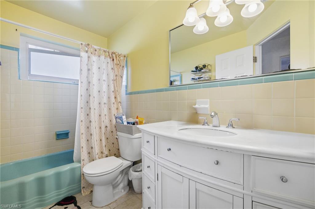 Full bathroom with vanity, shower / tub combo, tile walls, light tile patterned floors, and wainscoting