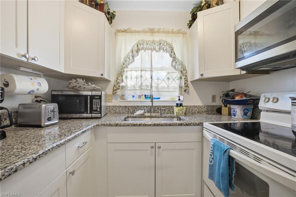 Kitchen featuring white electric stove, stainless steel microwave, white cabinets, and light stone countertops