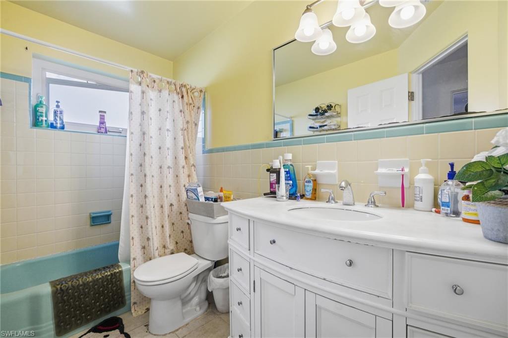 Full bath with vanity, shower / tub combo, tile walls, light tile patterned floors, and a wainscoted wall