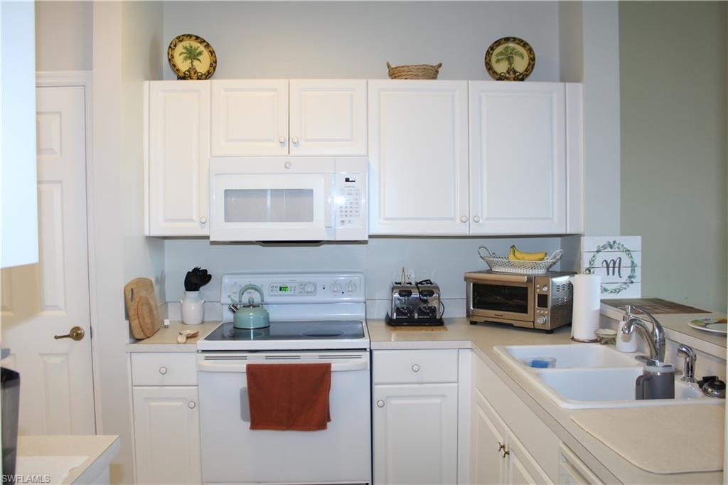 Kitchen featuring white appliances, white cabinetry, and light countertops
