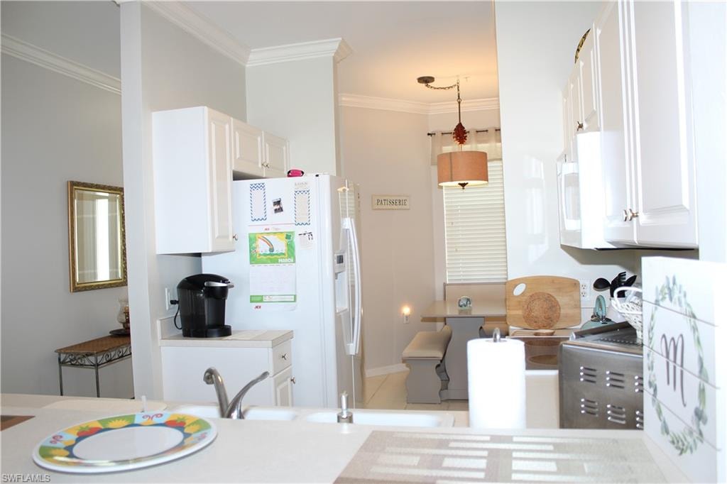 Kitchen featuring white cabinetry, white appliances, light countertops, crown molding, and hanging light fixtures