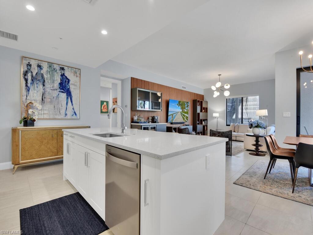 Kitchen featuring white cabinets, stainless steel dishwasher, a kitchen island with sink, light stone countertops, and a chandelier