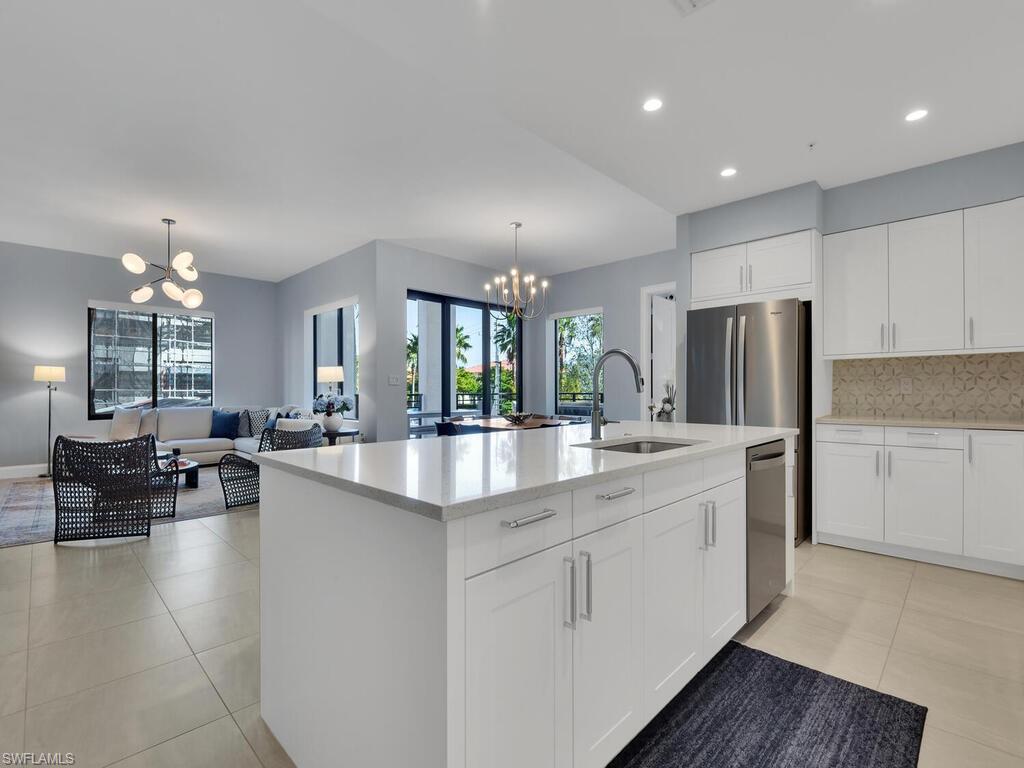 Kitchen with a chandelier, white cabinetry, stainless steel appliances, a center island with sink, and light stone countertops