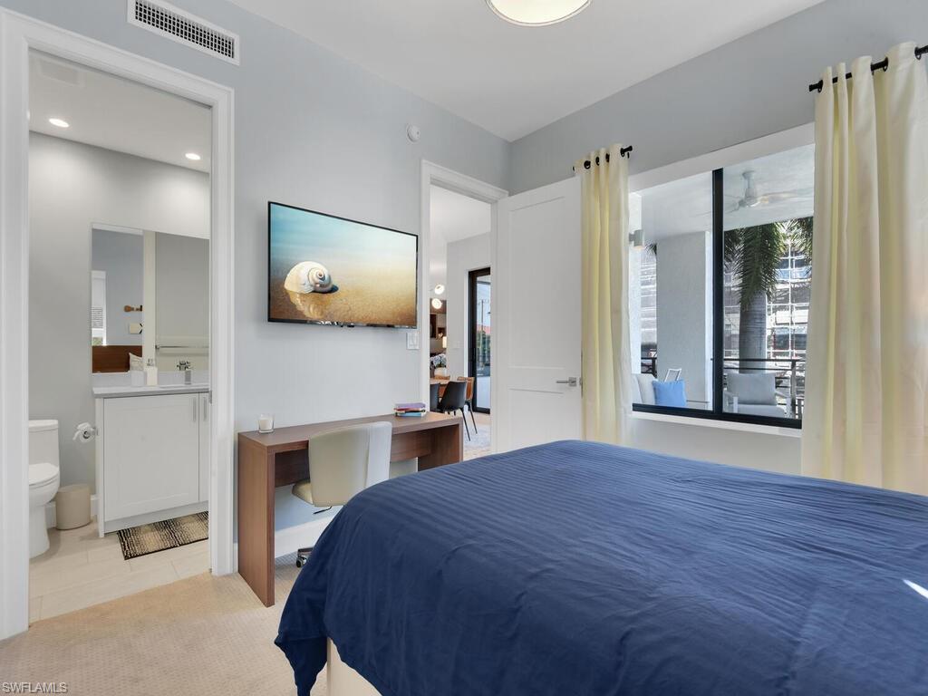 Bedroom with an office area, connected bathroom, and light carpet