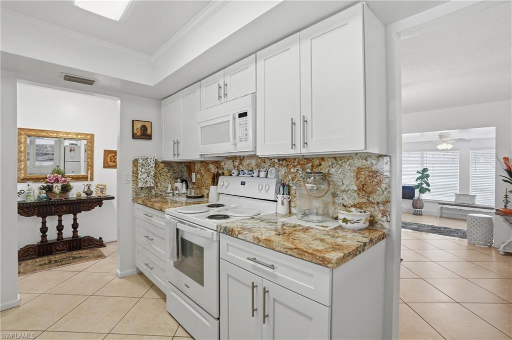 Kitchen featuring white appliances, white cabinetry, light tile patterned flooring, crown molding, and decorative backsplash