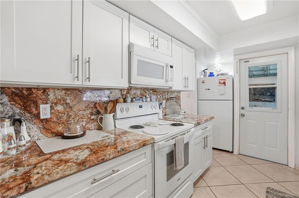 Kitchen with white appliances, white cabinetry, backsplash, ornamental molding, and light tile patterned flooring