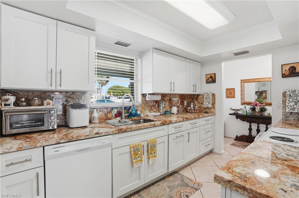 Kitchen featuring a tray ceiling, ornamental molding, white dishwasher, light stone counters, and white cabinetry