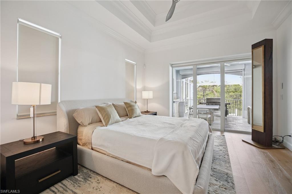 Primary bedroom on ground floor with slider access to lanai light wood floors, raised tray ceiling, and ornamental molding