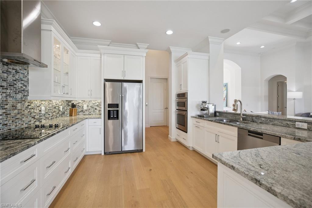 The kitchen has stainless steel appliances, spacious  counter space, white cabinets, attractive backsplash, and wood floor